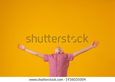 cheerful boy of about 8 years old in a red checkered shirt spread his arms out to the sides and smiled happily on yellow background. Close-up. boy rejoices in success and victory. Discounts and sales