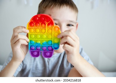 Cheerful boy holds in his hands a multi-colored toy anti-stress pop it in the form of Among Us.