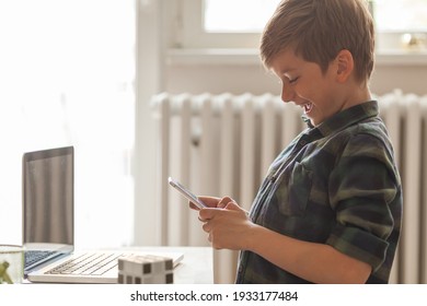 Cheerful Boy Laughing To A Text Message He Has Received Over Cell Phone At Home.