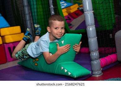 A Cheerful Boy Lies On A Soft Green Crocodile In A Children's Play Center