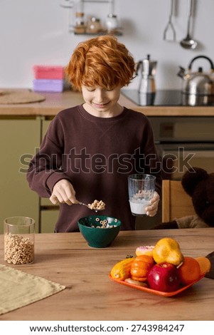 Cheerful boy smiles while preparing his breakfast with cereal and a tall glass of milk at home.