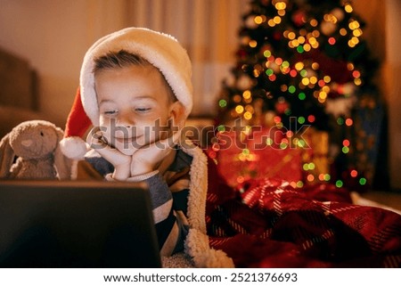 A cheerful boy is smiling at tablet while celebrating christmas and new year's eve at home.