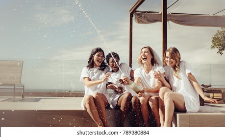 Cheerful bride and bridesmaids celebrating hen party with champagne while sitting on rooftop. Girls having a great time at the hen party. - Powered by Shutterstock