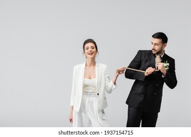 Cheerful Bride Looking At Camera Near Scared Arabian Groom With Slip Knot On Neck Isolated On Grey