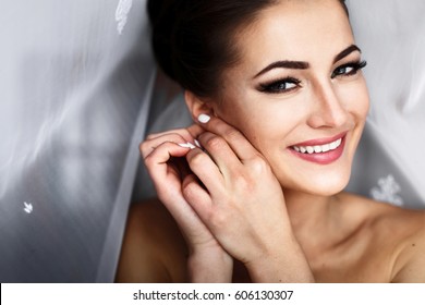 Cheerful bride smiles bride putting earring behind the curtain