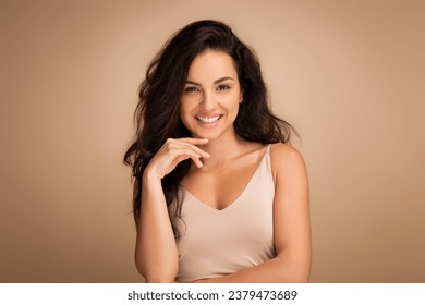 Cheerful brunette millennial middle eastern woman showcasing her natural beauty in a graceful pose against a seamless studio background, showing beautiful skin and long hair