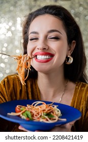 Cheerful Brunette Woman Holding Blue Plate And Fork With Pasta On Shiny Background