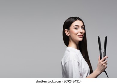 Cheerful Brunette Woman Holding Hair Straightener Isolated On Grey