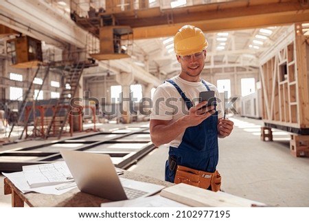 Cheerful builder using smartphone at construction site