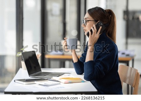 Cheerful business Asian woman freelancer making telephone call share good news about project working in office workplace, business finance concept.	