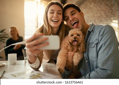 Cheerful Business Couple Having Fun With Their Dog And Taking Selfie With Mobile Phone In The Office. 