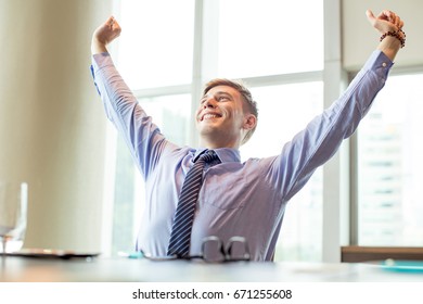 Cheerful Business Man Raising Arms at Office Desk