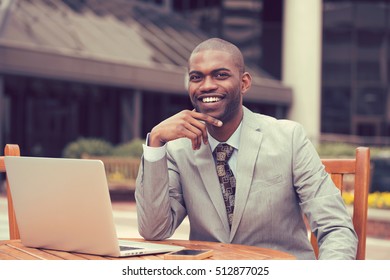 Cheerful Business Man In A Stylish Suit Sitting At Table With Laptop Outside Corporate Office Block Looking At The Camera With A Happy Face Expression