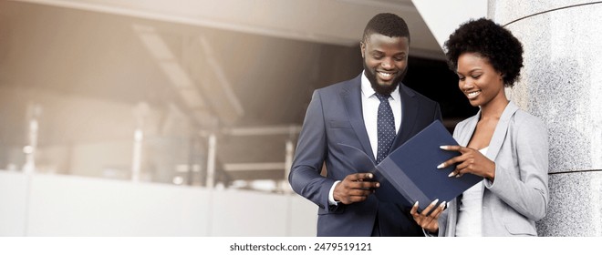 Cheerful businessman and businesswoman working while standing outdoors, reading financial reports. - Powered by Shutterstock