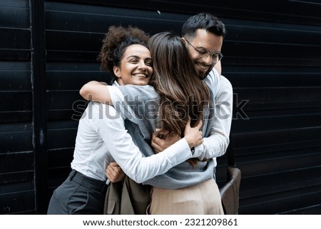 Cheerful businessman and businesswomen hugging each other in front of office building. Colleagues hug colleague who change her job and work, going to another company.