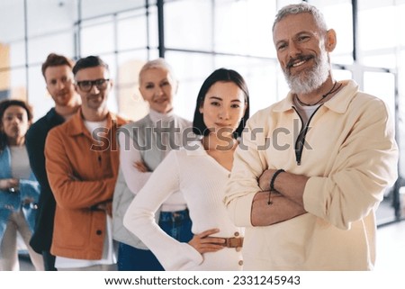 Cheerful businessman with crossed hands smiling during daytime for collaborative brainstorming with involved employees in association synergy, happy Caucasian male boss enjoying crew teamwork