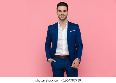 Cheerful businessman holding his hand in his pocket and laughing while wearing blue suit and standing on pink studio background