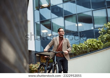 A cheerful businessman pushing his bicycle and going home from work, looking satisfied.