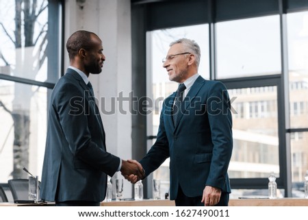 cheerful businessman shaking hands with african american diplomat