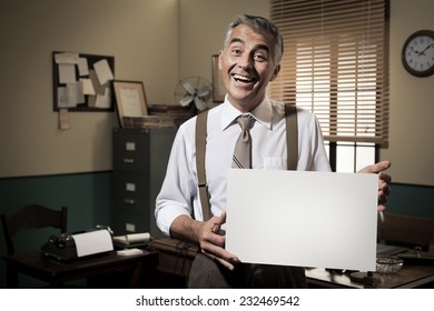Cheerful businessman showing a blank sign and smiling, 1950s office on background.