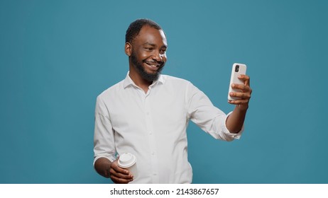 Cheerful businessman taking pictures on mobile phone, posing with coffee cup on camera. Happy freelancer using smartphone to take photos on coffee break, enjoying modern technology. - Powered by Shutterstock