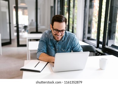 Cheerful businessman using laptop in bright office space.