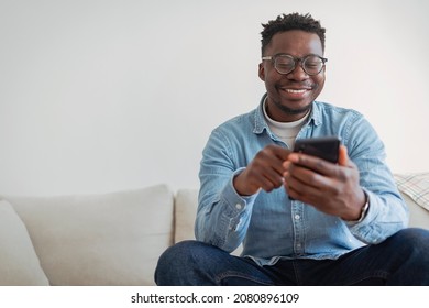 Cheerful Businessman Using Smartphone While Sitting On Sofa At Home. Closeup Of Mature Black Man Using Smartphone To Checking Email At Home. Happy African American Man Using Phone Mobile At Home.