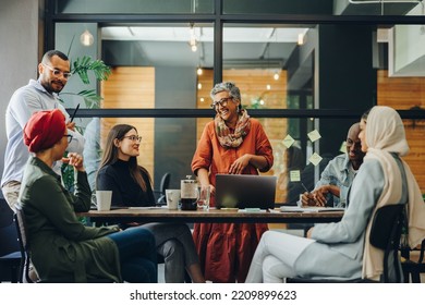 Cheerful businesspeople smiling happily during a meeting in a creative office. Group of successful business professionals working as a team in a multicultural workplace. - Powered by Shutterstock