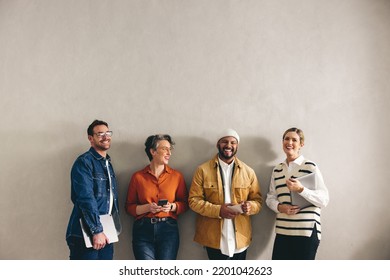 Cheerful businesspeople smiling happily while waiting in line for an interview. Group of shortlisted job applicants holding different digital devices in a modern office. - Shutterstock ID 2201042623