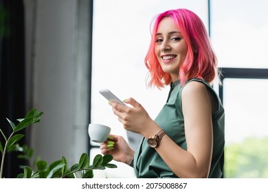 cheerful businesswoman with pink hair and piercing holding cup of coffee and smartphone - Powered by Shutterstock