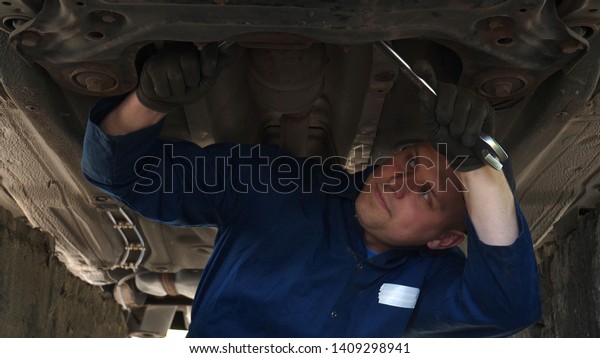 A cheerful car repairman on the street repairs\
the engine and lower part of the car, shows different emotions,\
dances with a big wrench.  
