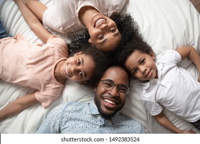 Cheerful carefree african full family lying down on bed smiling looking at camera feels happy spending time together close up top view portrait, responsibility, parentage, devotion endearment concept - Powered by Shutterstock