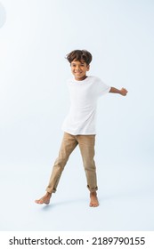 Cheerful carefree Indian boy swinging his arms back against bluish white background. He is wearing white T shirt. looking at the camera. - Shutterstock ID 2189790155