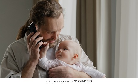 Cheerful Carefree Middle-aged Caucasian Man Bearded Father Answering Call Talking To Wife Mom With Phone Online Order Booking Baby Food Holding Little Daughter Newborn Infant At Home Chatting Friendly