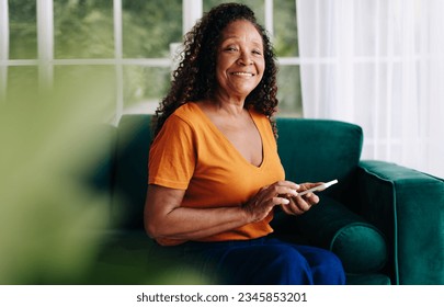 Cheerful and carefree senior woman sitting on a couch and using her smartphone as an essential tool for accessing mobile apps, enhancing her day-to-day life and staying informed at home. - Powered by Shutterstock