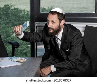 Cheerful and carefree successful, caucasian rich businessman in office throwing money, playing with cash Israel NIS banknotes, sitting pleased with delighted face. Concept for money and success.