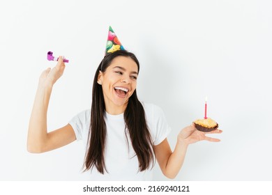 Cheerful Carefree Young Woman In Party Cap Celebrating Birthday Dancing With Kazoo Pipe And Cake In Her Hands, White Background