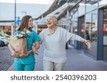 A cheerful caregiver helps a joyful elderly woman with groceries. The scene captures warmth, companionship, and supportive care in an outdoor shopping environment.