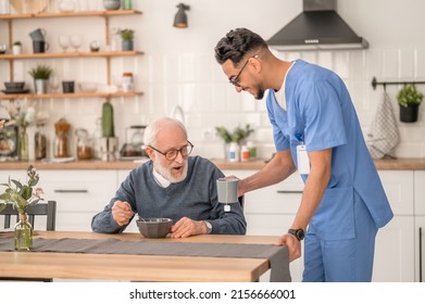 Cheerful caregiver serving tea to an aged man - Powered by Shutterstock