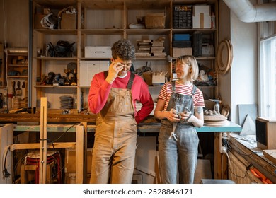 Cheerful carpenter couple laughs, goofs off during break in workshop. Family business, teamwork, shared passion, creative collaboration, small business, work life balance, joyful working partnership - Powered by Shutterstock