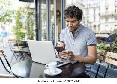 Cheerful casual man working on laptop in cafe terrace. Businessman texting on smartphone outdoor in the city - Powered by Shutterstock