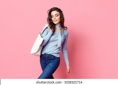 Cheerful casual young woman with bag looking away on pink background.