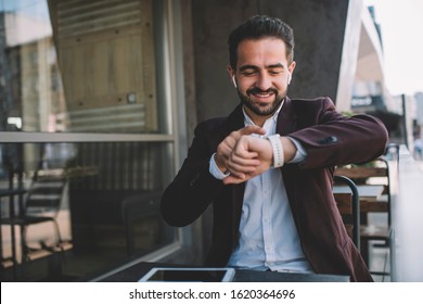 Cheerful caucasian bearded businessman sitting on cafe terrace using modern digital devices for checking mails and notification,smiling young man in formal wear looking at his wristwatch display
 - Powered by Shutterstock