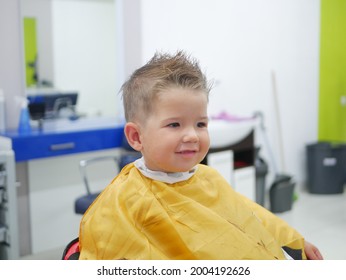 Cheerful Caucasian boy toddler happy to be on the haircut with a professional children's hairdresser. Brunet little boy having a haircut at hair salon. High quality photo