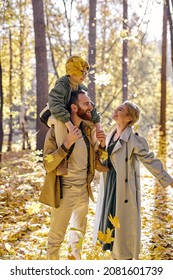 cheerful caucasian european woman throwing yellow autumn leaves have fun with husband and son, in the park or forest, outdoors. leisure, holidays, weekends, parenthood, family concept.