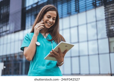 A cheerful Caucasian female nurse in teal scrubs actively engages with a tablet outside a medical facility, her focus on the screen enhancing healthcare communication. - Powered by Shutterstock