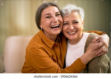 Cheerful Caucasian female pensioners looking at camera with happy carefree smiles, sitting comfortably on sofa, embracing each other, telling jokes, recollecting good old stories, having fun
 - Powered by Shutterstock