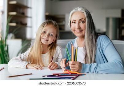 Cheerful caucasian little girl with aged lady with colorful pencils draw a picture on table, enjoy study and free time in living room interior. Art lesson together, education and entertainment at home - Shutterstock ID 2201003573