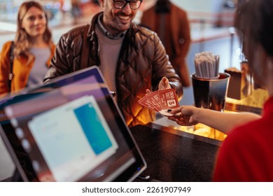 A cheerful Caucasian man is at the cash register in the movie theater buying tickets from the theater clerk. - Shutterstock ID 2261907949