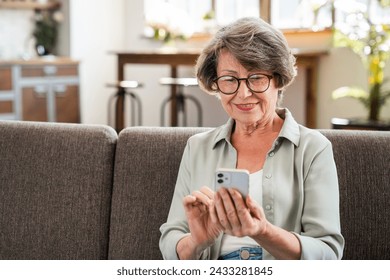 Cheerful caucasian senior woman using cellphone while relaxing on the sofa couch at home. Online shopping, scrolling social media, paying bills in mobile application - Powered by Shutterstock